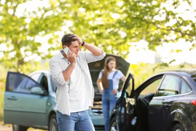 A man stands beside a car, talking on his cell phone with a focused expression.